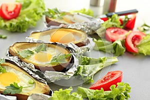 Avocado baked with eggs in foil and fresh vegetables on table