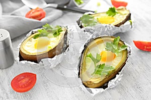 Avocado baked with eggs in foil on wooden table