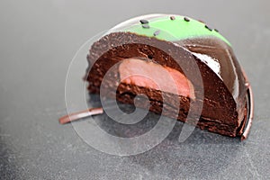 Avocado and chocolate mousse dessert with mirror glaze and black sesame seeds on scratched steel table
