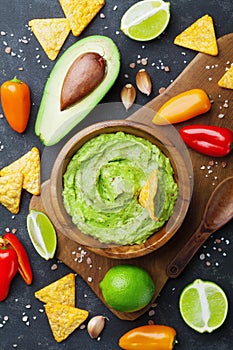 Avocado guacamole with ingredients pepper, lime and nachos on black table top view. Traditional mexican food. photo