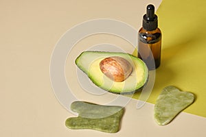 avocado half, amber glass dropper bottle and jade gua sha scrapers