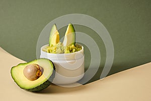 avocado half and white mockup blank jar with avocado puree on wooden stand, green background