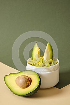 avocado half and white mockup blank jar with avocado puree on wooden stand, green background