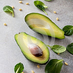 Avocado halves and baby spinach leaves on concrete, stone or slate background. Dietary food, concept of vegetarian food.