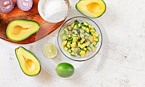 Avocado halves, limes and onion, some salt near - basic guacamole ingredients on white working board, view from above, space for