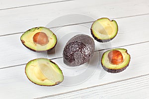 Avocado halves, and one whole fruit arranged on white boards desk