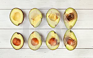 Avocado halves sorted from ripe to overripe on white boards desk, view from above