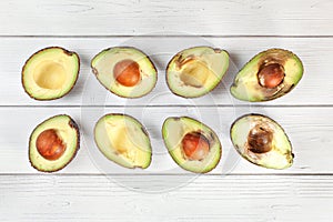 Avocado halves on white boards desk, view from above. Fruits arranged from unripe to overripe