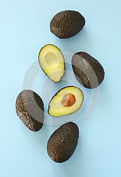 Avocado halves and whole on a light blue background.