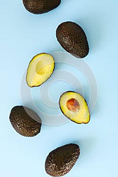 Avocado halves and whole on a light blue background.