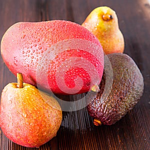 Avocado hass with red pears, ripe mango with water drops on a wooden table close-up, copy space, template