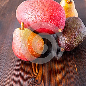Avocado hass with red pears, ripe mango with water drops on a wooden table close-up, copy space, template