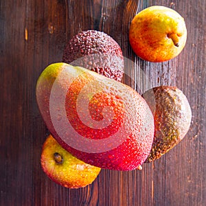 Avocado hass with red pears, ripe mango with water drops on a wooden table close-up, copy space, template