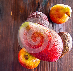 Avocado hass with red pears, ripe mango with water drops on a wooden table close-up, copy space, template