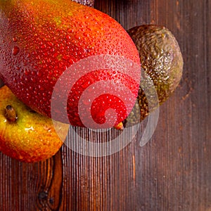 Avocado hass with red pears, ripe mango with water drops on a wooden table close-up, copy space, template