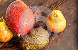 Avocado hass with red pears, ripe mango with water drops on a wooden table close-up, copy space, template