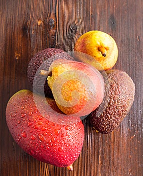 Avocado Hass with red pears, ripe mango with water drops on a wooden table close-up, copy space, template