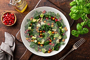 Avocado, kale, roasted chickpeas, almond and pomegranate salad in white bowl