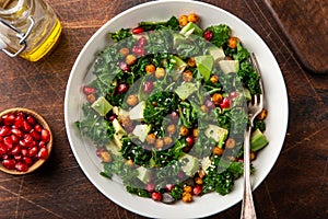 Avocado, kale, roasted chickpeas, almond and pomegranate salad in white bowl