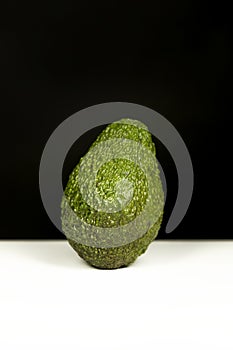 An avocado that is lacking time to be ripe on a white surface