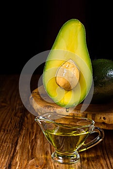 Avocado oil drops drain into a glass bowl. Avocado fruit and avocado oil on a wooden rustic tray on table