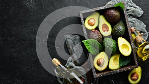 Avocado oil and fresh avocados on a black background. Rustic style. Top view.