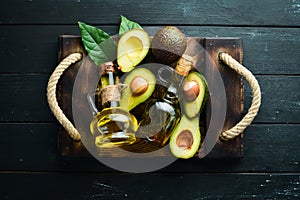 Avocado oil and fresh avocados on a black background. Rustic style. Top view. photo