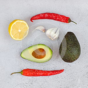 Avocado and red chilli peppers and lemon and garlic on grey background