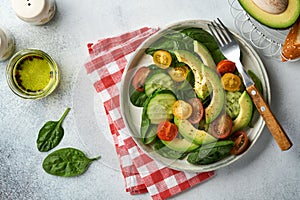 Avocado, red, yellow, black cherry tomato, spinach and cucumber fresh salad with spices pepper and olive oil in grey bowl on grey