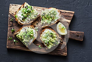 Avocado and ricotta toast with micro greens on a cutting board, on a dark background, top view. Good fats healthy eating concept.