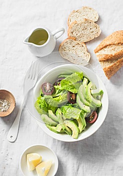 Avocado, romano, kumato tomatoes salad and whole wheat branny bread on light background, top view. Healthy diet vegetarian food