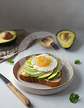 Avocado toast with egg on a plate and table with a fork, side view. Healthy breakfast