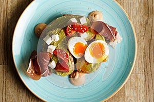 Avocado toast with guacamole, soft boiled egg, ham, cream cheese and tomatoes on a plate