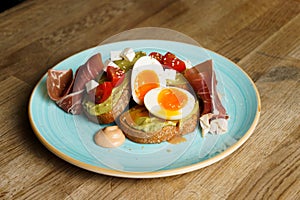 Avocado toast with guacamole, soft boiled egg, ham, cream cheese and tomatoes on a plate