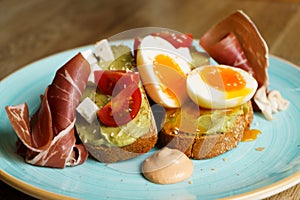 Avocado toast with guacamole, soft boiled egg, ham, cream cheese and tomatoes on a plate