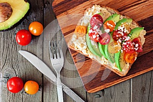 Avocado toast with hummus and tomatoes on server, above scene on wood