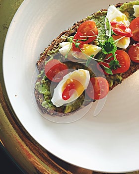 Avocado toast on plate with soft-boiled egg, cherry tomatoes, cilantro