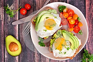 Avocado toasts with eggs and tomatoes, above view on dark wood