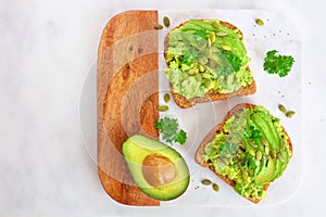 Avocado toasts with pumpkin and chia seeds, top view on a marble and wood platter