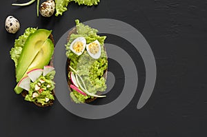 Avocado toasts on rye bread with sliced avocado for healthy breakfast on dark black stone background. Vegetarian food. Top view,