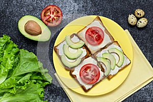 Avocado and tomato sandwich on a yellow plate. Lettuce leaf and quail egg on a dark board. Vegetarian food, dieting nutrition