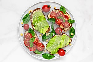 Avocado and tomatoes toasts with hummus, sesame and basil in a plate over white marble background. vegan food