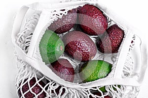 Avocado of two sorts in the mesh bag on the white table