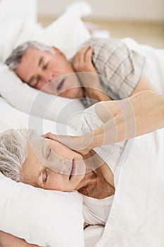 Awake senior woman in bed covering her ears