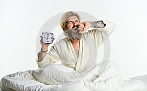 Awakening. Sleepy guy and alarm clock in bed. Bearded man with alarm clock. Sleep complex biological process that helps