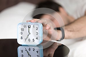 Awaking man in bed wearing wristband turning off alarm clock photo