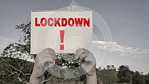 awareness concept - text lockdown and exclamation mark on notepad with hands holding it