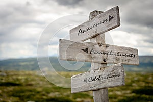 awarness, accomplishments and celebrations text on wooden signpost outdoors in nature.