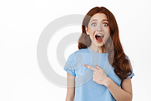 Awesome discounts. Amazed redhead girl gasp and say wow, checking out promo logo, pointing finger left and react to