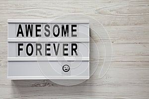 `Awesome forever` word on modern board on a white wooden background, top view. From above, flat lay, overhead. Copy space